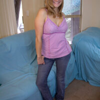 Barefoot blonde strips to her brassiere and thong on a chesterfield